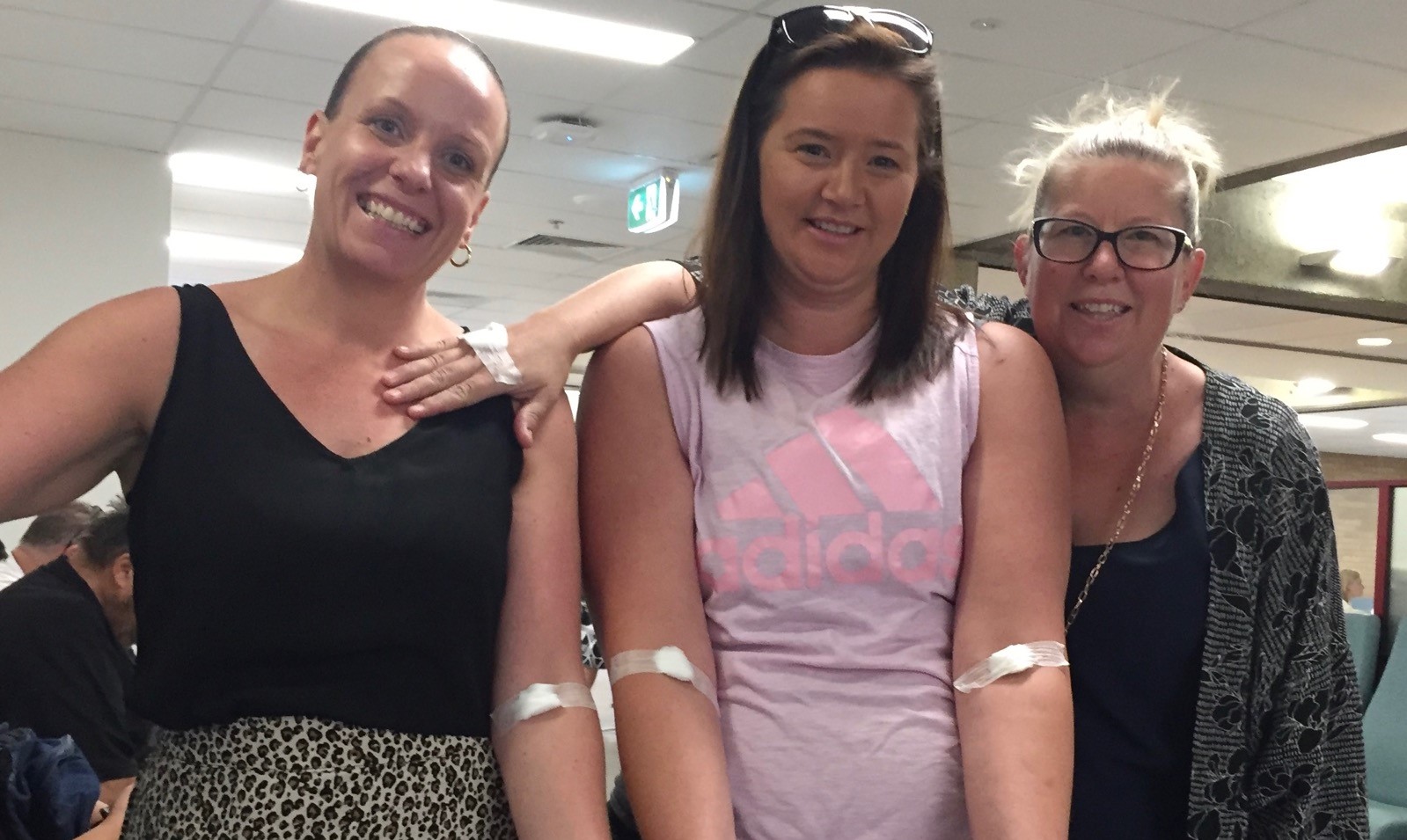Hume employee Karen stands between her sister Debbie and her best friend. They are holding their arms out to show the bandaid after their blood test.